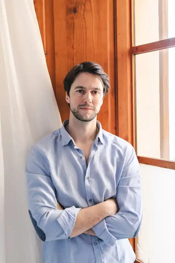 Andrew with arms crossed beside a wooden window frame