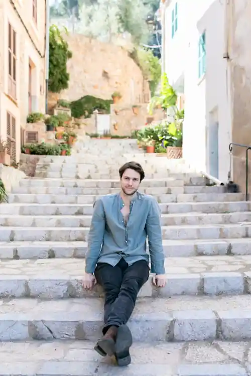 Andrew sitting on a stone staircase between white houses